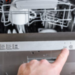 Close up of a man's hand choosing the setting on a full dishwasher.
