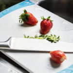Closeup of strawberries and a knife on a chopping board by a sink.