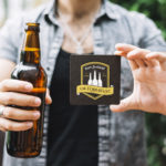 Man holding a beer bottle and a promotional melamine coaster.